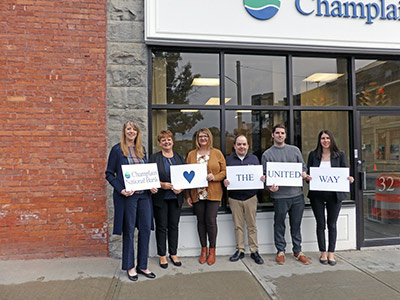 Five People Holding Signs Saying Champlain National Bank Loves The United Way