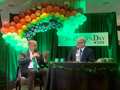 Two Men Holding Microphones Under a Balloon Rainbow