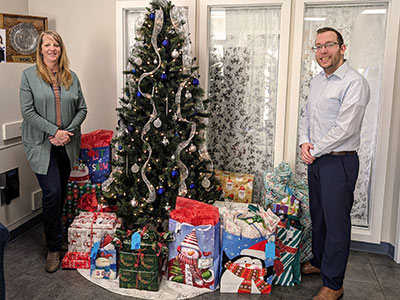 Two People Standing Next to a Christmas Tree with Lots of Wrapped Gifts Underneath