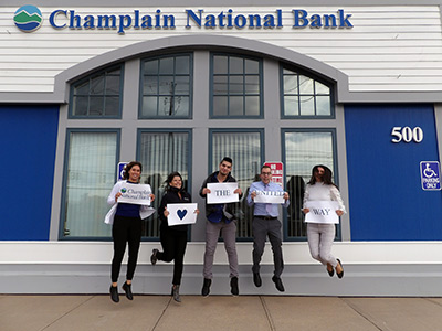 Five People Jumping While Holding a Sign that Says Champlain National Bank Loves the United Way