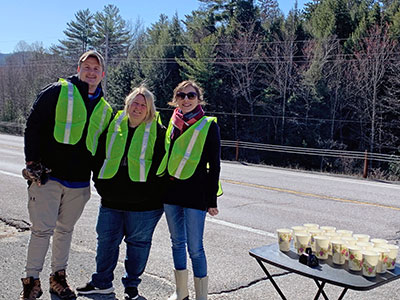 Three people wearing reflective vests next to a table of cups of water on the road