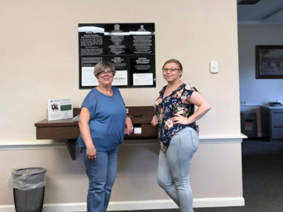 Two women wearing jeans standing next to the check writing station in Crown Point.