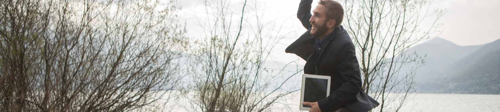 Man Jumping While Holding a Tablet in the Mountains