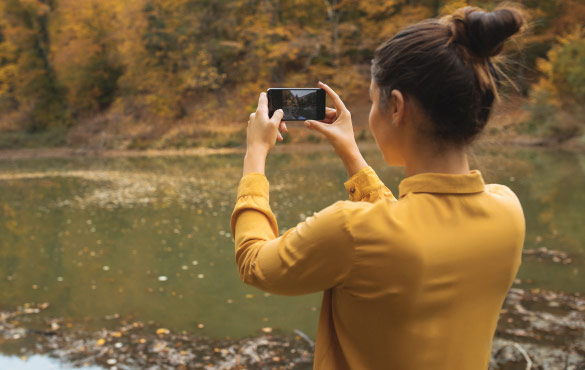 Girl Holding Phone Taking Picture of a Lake