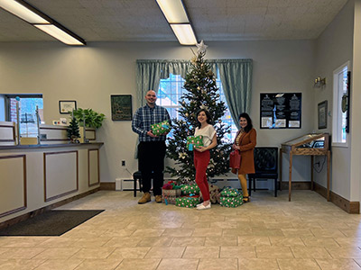 Three People Holding Wrapped Christmas Presents Next to a Tree